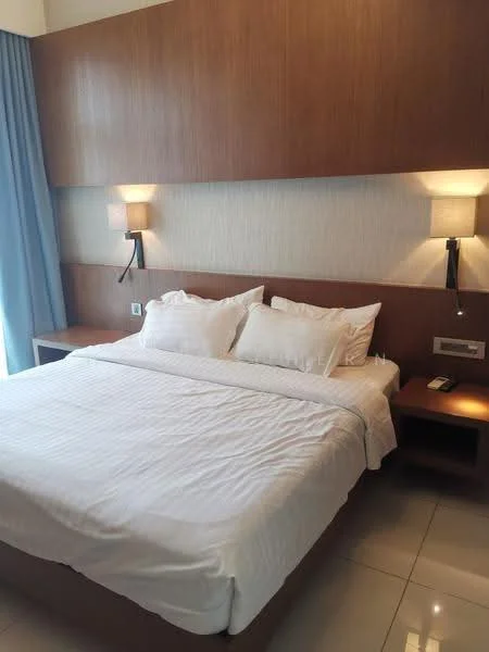 Bedroom features: king-size bed with white bedding, wooden headboard, two bedside tables, wall-mounted reading lamps, light-colored wallpaper, floor-to-ceiling window with blue curtains, glossy tile flooring, built-in wall paneling; style: modern.