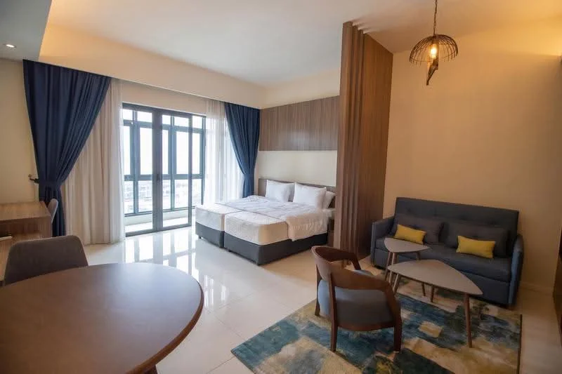 Bedroom features: two single beds with white bedding, wooden headboard, floor-to-ceiling windows, sheer curtains, dark blue drapes, laminate flooring, recessed downlights, pendant light fixture, sofa in grey fabric, coffee table, area rug with geometric pattern, dining table, chairs, built-in wardrobe; style: modern; view: city.