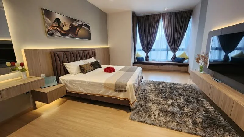 Bedroom features: king-size bed with upholstered headboard, white bedding with decorative throw, wooden bedside tables, table lamp on bedside table, large area rug with shaggy texture, wall-mounted TV, built-in wardrobe, floor-to-ceiling windows with sheer curtains, grey accent wall, decorative flowers in vase, window seat with cushions; style: modern; view: city.
