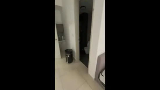 Room features: white painted walls, light-colored tile flooring, recessed ceiling lights, doorway leading to bathroom, black trash bin, toilet visible through doorway.
