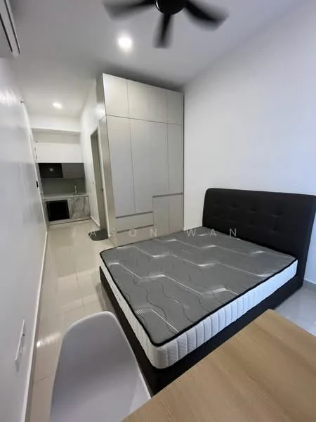 Bedroom features: queen-size bed with grey mattress, black upholstered headboard, white walls, glossy tile flooring, ceiling fan, built-in wardrobe with sliding doors, small dining table, white chair, kitchenette visible in background; style: modern.