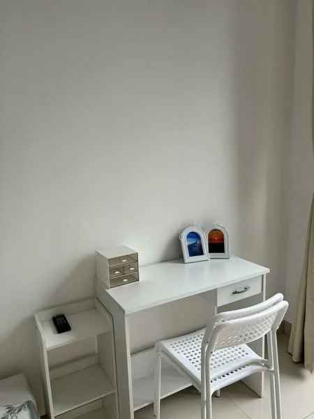 Study features: white desk with drawer, white chair with perforated seat, small white storage unit, two decorative frames, light-colored walls, tile flooring, curtains, remote control on surface; style: minimalist.
