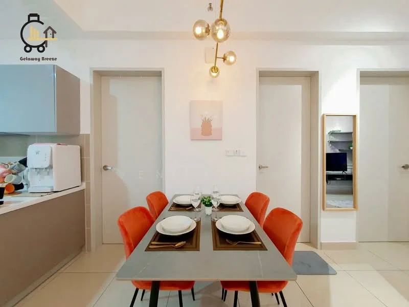 Dining features: rectangular dining table, grey tabletop, 4 orange upholstered dining chairs, decorative centerpiece with greenery, wall-mounted mirror, neutral wall colour, recessed lighting, pendant light fixture with multiple bulbs; style: modern. Kitchen features: light grey cabinetry, white countertop, built-in microwave, white kettle, stainless-steel sink, chrome faucet, open shelving, tile flooring; style: modern. Room features: white painted walls, two doors leading to other rooms.