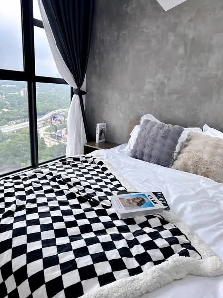 Bedroom features: king-size bed, white bedding, black and white checkered throw blanket, grey decorative pillows, floor-to-ceiling windows, curtains in dark blue, concrete accent wall, nightstand with a book, view of the city skyline; style: modern; view: city.