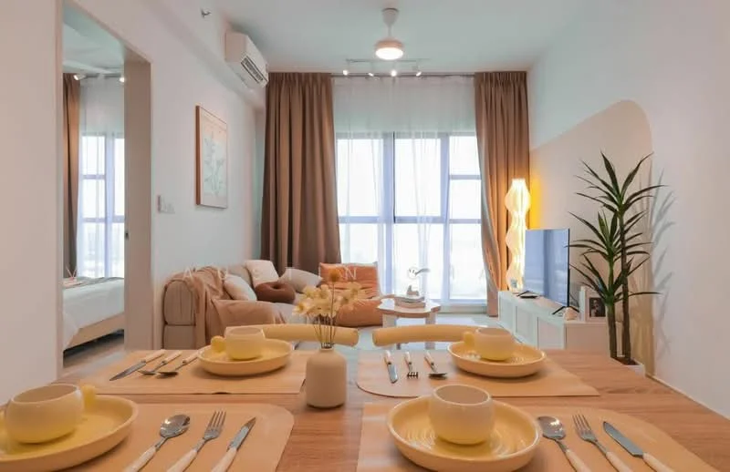 Dining features: wooden dining table, yellow dinner plates, cutlery set, decorative vase with flowers, table runner, 4 dining chairs, light wood flooring, recessed ceiling lights; style: modern; view: city. Living features: beige fabric sofa, floor lamp, wall-mounted TV, white TV console, decorative plant, curtains, large windows, artwork on wall; style: modern; view: city. Room features: bed with bedding, curtains, wall-mounted air conditioning unit.