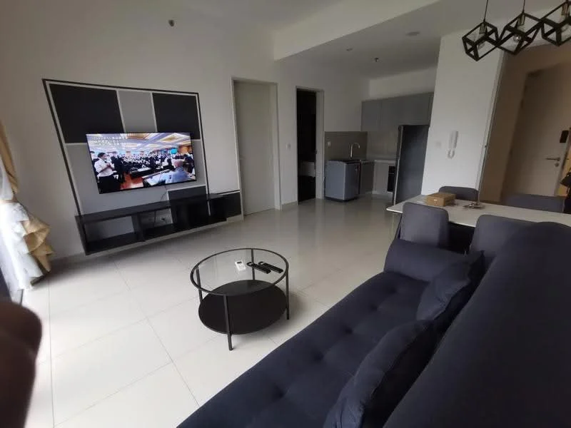 Living features: 3-seater fabric sofa in navy blue, coffee table with black metal frame, wall-mounted TV, TV console in black, white walls, tile flooring, curtains in light color, recessed lighting, open layout to kitchen, decorative wall art; style: modern. Kitchen features: stainless-steel fridge, built-in oven, freestanding range oven, grey cabinetry, countertop with backsplash, sink, kitchen island, tile flooring; style: modern.
