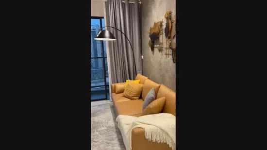 Living features: 3-seater leather sofa in tan, yellow accent cushions, grey patterned throw pillow, floor lamp with arching arm, decorative wall art with map design, curtains in light grey, textured wall in grey, area rug with geometric pattern, floor-to-ceiling windows, view of city skyline; style: modern; view: city.
