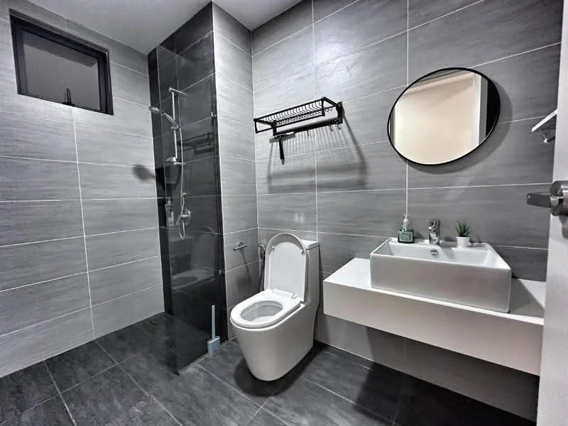 Bathroom features: grey tiled walls, dark grey tiled flooring, walk-in shower with glass enclosure, rain shower head, handheld shower, white wall-mounted sink, chrome basin mixer faucet, one-piece toilet, round mirror, black wall-mounted towel rack, small potted plant; style: modern.