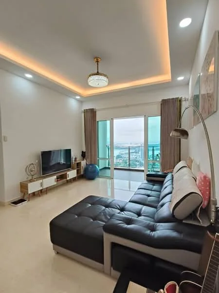 Living features: L-shape sectional sofa in black leather, coffee table, TV console, wall-mounted TV, floor-to-ceiling windows, sliding glass door, curtains, recessed downlights, chandelier, lighted ceiling with cove lighting, decorative wall art, ceramic tile flooring; style: modern; view: city.