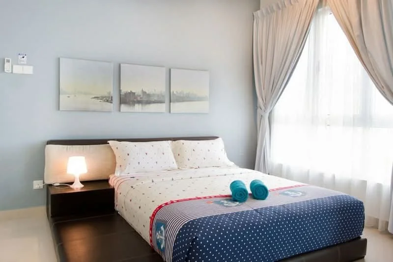 Bedroom features: queen-size bed with white bedding, blue polka dot bedspread, two blue towels on bed, nightstand with lamp, floor-to-ceiling windows, sheer curtains, painted light blue walls, framed artwork on wall, light-colored tile flooring; style: modern; view: city.