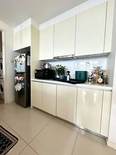 Kitchen features: cream high-gloss cabinetry, white countertop, stainless-steel fridge, built-in microwave, black sink, chrome faucet, kettle, decorative plants, countertop storage jars, laundry appliances visible in background, tile flooring; style: modern.