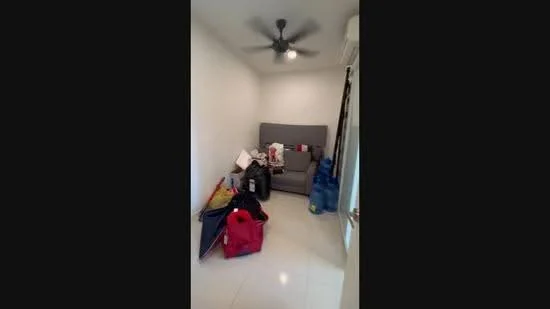 Room features: white painted walls, tile flooring, 5-blade ceiling fan, grey fabric sofa, various bags and items on the floor, window with curtain, air conditioning unit.