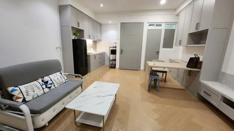 Living features: grey fabric sofa, decorative cushions with geometric patterns, marble coffee table, light wood flooring, built-in cabinetry with grey finish, white countertop, black refrigerator, kitchen area with white cabinetry, window with natural light, dining table with light wood finish, blue chair, wall-mounted TV console; style: modern.