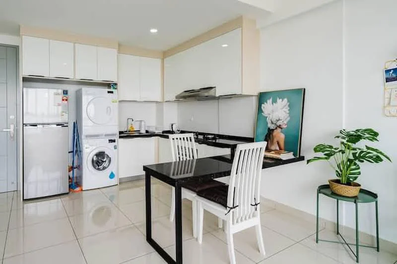 Kitchen features: white glossy cabinetry, black countertop, stainless-steel sink, chrome pull-down faucet, built-in oven, freestanding washing machine, freestanding dryer, 4-burner gas hob, refrigerator, white tiled backsplash, white ceramic tile flooring, dining table with black surface, 4 white dining chairs, houseplant in ceramic pot; style: modern.