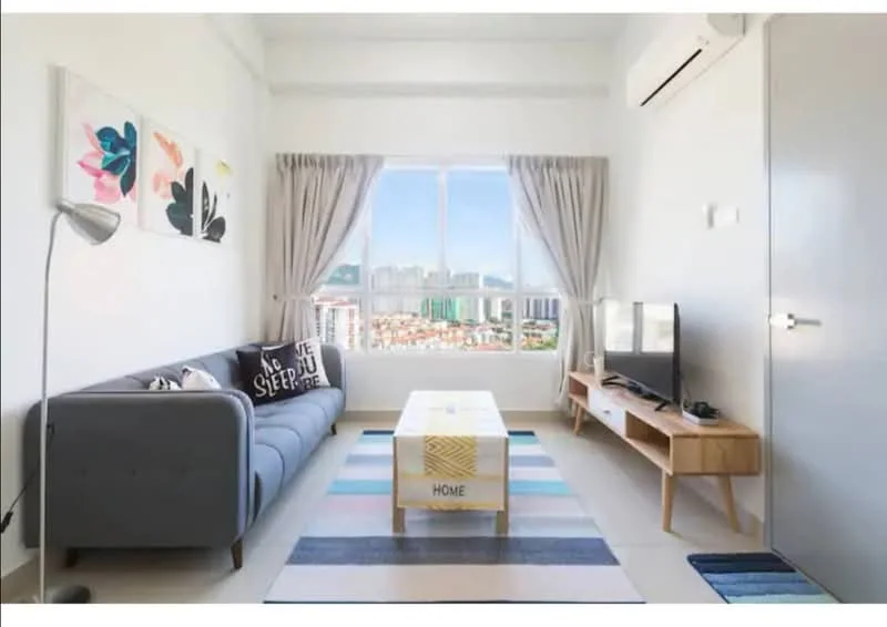 Living features: grey fabric sofa, decorative cushions, coffee table with patterned runner, wall-mounted TV, wooden TV console, floor lamp, curtains, air conditioning unit, city skyline view through window, light-colored walls, neutral flooring; style: modern; view: city.