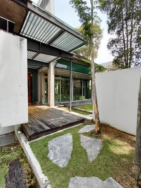 Exterior type: detached bungalow; features: wooden deck pathway, stone stepping stones, manicured lawn, glass facade, exposed concrete walls, overhanging roof with metal awning, surrounded by greenery, landscaped garden; style: modern.