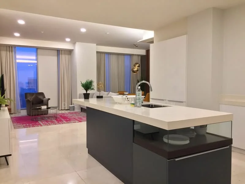 Kitchen features: island kitchen with white countertop, stainless-steel sink, chrome pull-down faucet, built-in cabinetry, marble tile flooring, recessed downlights, floor-to-ceiling windows, plant decoration, open layout to living area, grey cabinetry, decorative wall art, area rug with geometric pattern; style: modern; view: city. Living features: armchair, coffee table, area rug, floor-to-ceiling windows, decorative plant; style: modern; view: city.