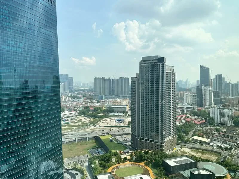 Exterior type: high-rise condominium; features: glass curtain wall, surrounded by urban skyline, green landscaping at base, nearby sports field, multiple high-rise buildings in view, city skyline in background; style: modern.