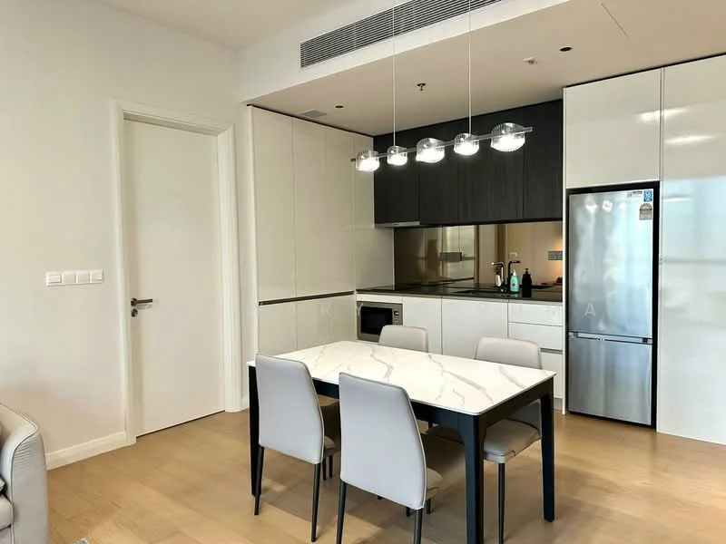 Dining features: 6-seater dining table with marble top, upholstered dining chairs in light grey, white cabinetry with flat-panel design, black countertop, built-in oven, stainless-steel fridge, glass backsplash, pendant lighting with multiple bulbs, light wood flooring, white painted walls, door leading to hallway; style: modern.