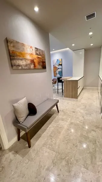 Room features: marble tile flooring, light grey painted walls, recessed downlights, framed artwork on wall, bench with cushion, wooden accent table, open kitchen layout visible in background, neutral color palette; style: modern.