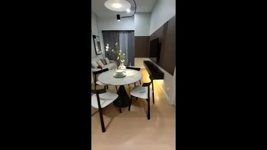 Dining features: round dining table with marble top, 4 white upholstered dining chairs, decorative centerpiece with flowers, wall-mounted TV, light wood flooring, grey curtains, accent wall with dark wood paneling, recessed lighting, sofa in background, open layout to living area; style: modern.