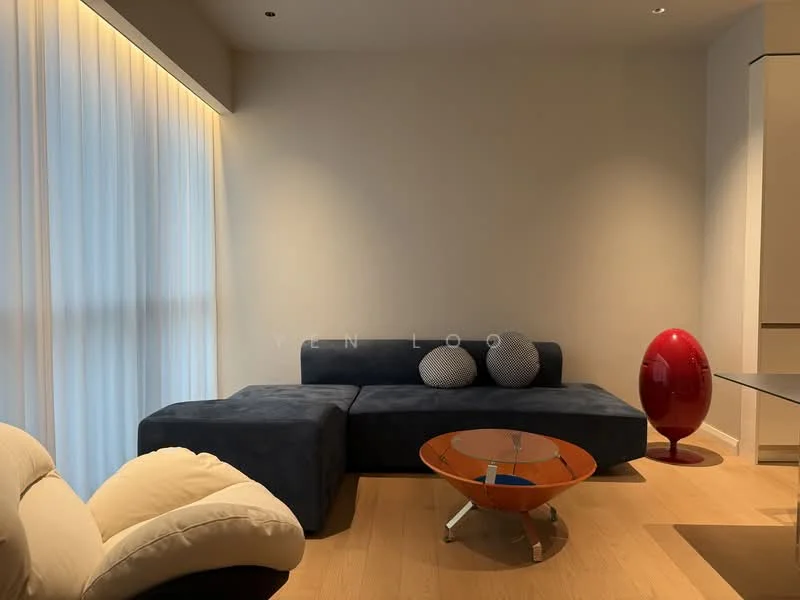 Living features: L-shape sectional sofa in navy blue, two decorative cushions on sofa, glass coffee table with orange base, light wooden flooring, floor-to-ceiling windows with sheer curtains, accent chair in cream fabric, red decorative sculpture, neutral painted walls; style: modern.