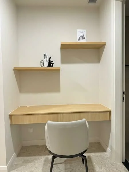 Study features: light wood desk with drawer, white upholstered chair, two floating shelves, white painted walls, neutral flooring, decorative items on shelves, minimalist decor; style: modern.