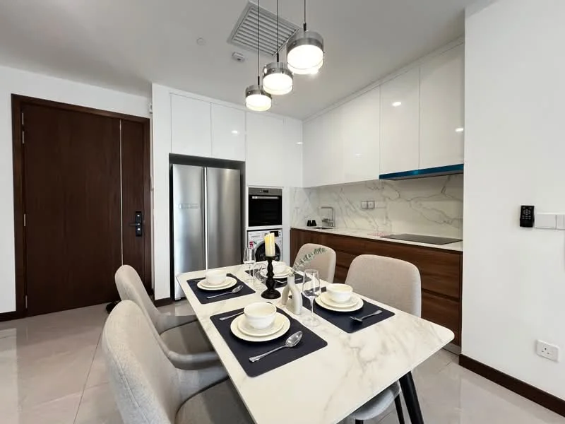 Kitchen features: white glossy cabinetry, wooden cabinetry, marble countertop, stainless-steel fridge, built-in oven, induction cooktop, single-bowl stainless-steel sink, chrome pull-down faucet, pendant lighting, dining table with marble top, upholstered dining chairs, table setting with plates and cutlery, wall-mounted kitchen cabinet, tile backsplash; style: modern.