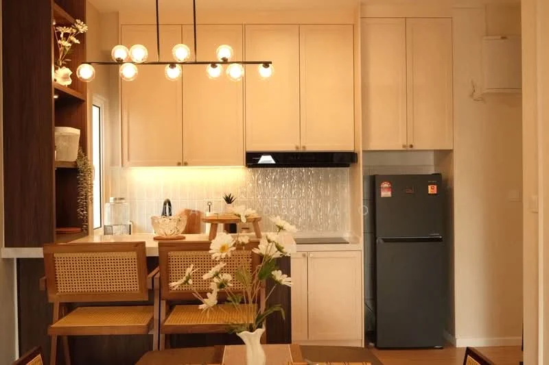 Kitchen features: white shaker cabinets, black countertop, stainless-steel sink, chrome pull-down faucet, built-in oven, stainless-steel fridge, pendant light fixture with multiple bulbs, glass tile backsplash, bar seating with cane chairs, wooden dining table, decorative vase with flowers; style: modern.