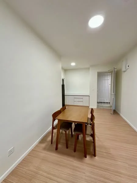 Dining features: wooden dining table, 4 wooden dining chairs, light-colored laminate flooring, white painted walls, recessed ceiling lights, wall-mounted split AC; style: modern. Kitchen features: white cabinetry, countertop with sink, refrigerator visible in background; style: modern.