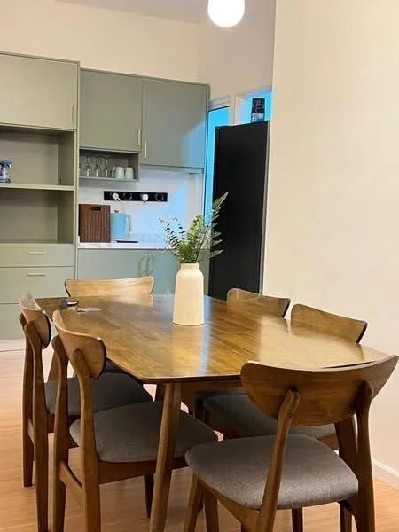 Dining features: wooden dining table, 4 wooden dining chairs with grey upholstery, vase with greenery on table, light fixture hanging from ceiling, open kitchen area visible in background, green cabinetry in kitchen, black refrigerator, white walls, laminate flooring; style: modern.