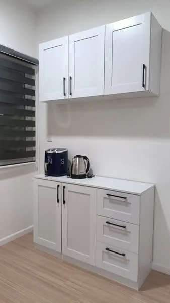 Room features: white cabinetry with flat-panel doors, silver handles on cabinets and drawers, white countertop, kettle, blue container, laminate flooring, grey roller blinds, white painted walls; style: modern.