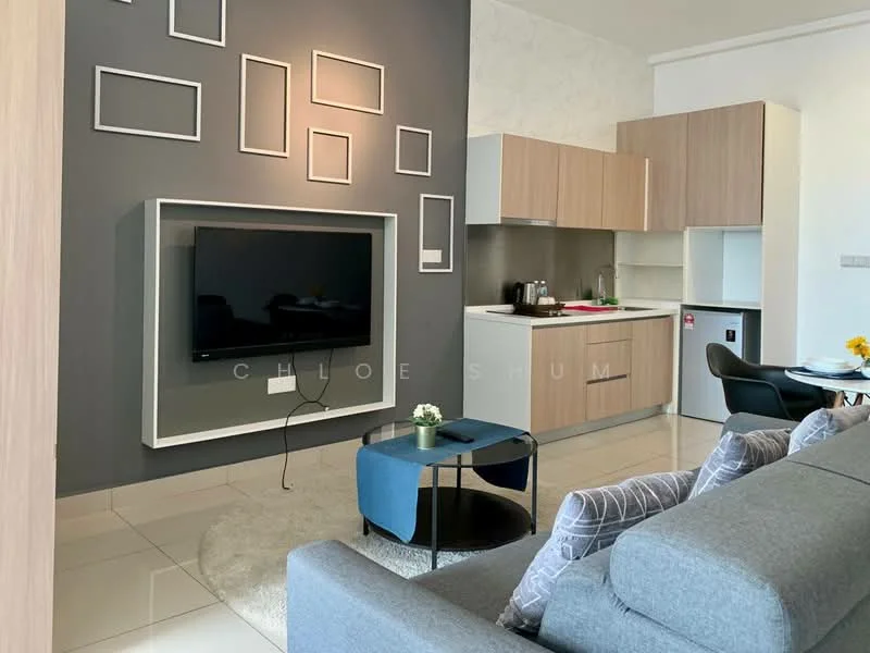 Living features: grey fabric sofa, round blue coffee table, area rug, wall-mounted flat-screen TV, light wood cabinetry, white countertop, kitchen appliances visible, white walls, grey accent wall with picture frames, refrigerator, sink, kettle, decorative flower vase; style: modern.