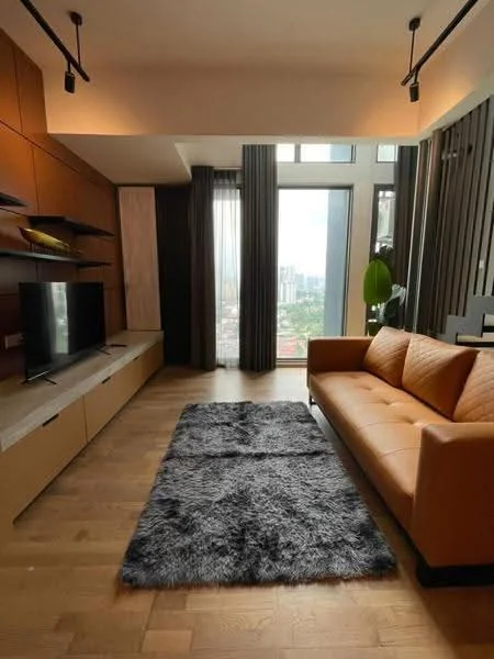 Living features: 3-seater leather sofa in orange, TV console, wall-mounted TV, wooden flooring, area rug with shaggy texture, floor-to-ceiling windows, curtains, decorative plant, shelves with decorative items, accent wall with wood paneling, recessed lighting; style: modern; view: city.