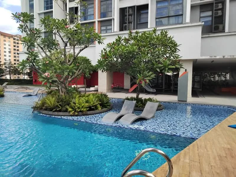 Exterior type: swimming pool deck; features: infinity pool, pool deck with loungers, tropical landscaping, plumeria trees, manicured garden beds, blue mosaic tile pool, wooden decking, surrounding residential buildings, sun loungers, shaded seating area; style: modern.