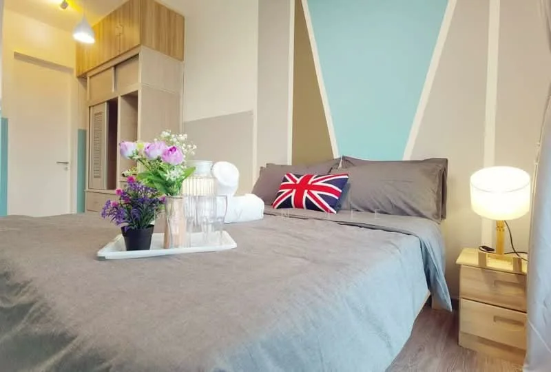 Bedroom features: queen-size bed with grey bedding, decorative pillow with Union Jack design, nightstand with lamp, wooden flooring, built-in wardrobe with sliding doors, accent wall with geometric design in blue and beige, decorative tray with flowers and towels, wall-mounted light fixture; style: modern.