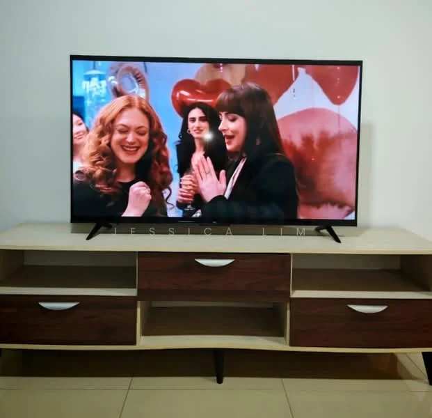 Room features: flat-screen TV, wooden TV console with drawers, cream-colored walls, beige tiled flooring, decorative wall art, red and pink balloons in background; style: modern.