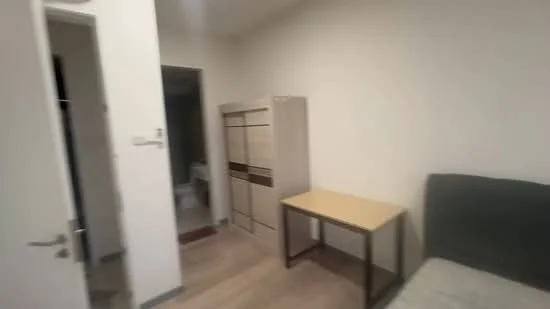 Room features: light-colored painted walls, laminate flooring, wooden wardrobe with sliding doors, simple wooden table, single bed, door leading to bathroom, minimalist decor; style: modern.