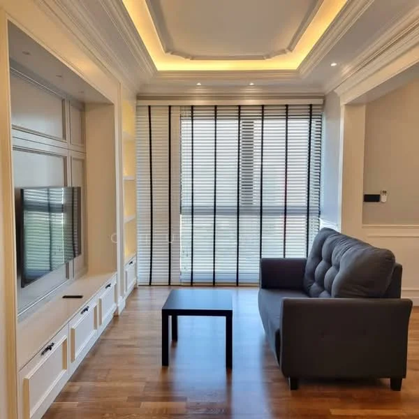 Living features: grey fabric sofa, black coffee table, wall-mounted TV, built-in cabinetry with white finish, recessed downlights, crown moulding on ceiling, wooden flooring, floor-to-ceiling windows with black horizontal blinds; style: modern.