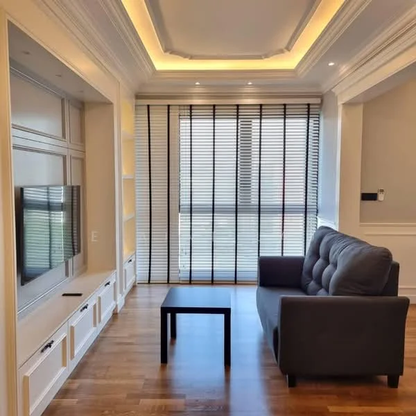 Living features: grey fabric sofa, black coffee table, wall-mounted TV, built-in cabinetry, recessed downlights, crown moulding, wooden flooring, floor-to-ceiling windows with blinds; style: modern; view: city.