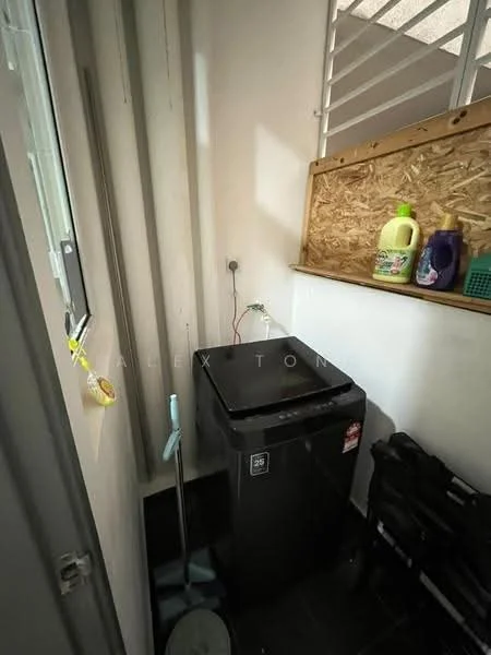 Laundry features: black top-loading washing machine, white walls, black tile flooring, wooden shelving, cleaning supplies on shelf, mop and bucket, window with security bars, laundry basket.
