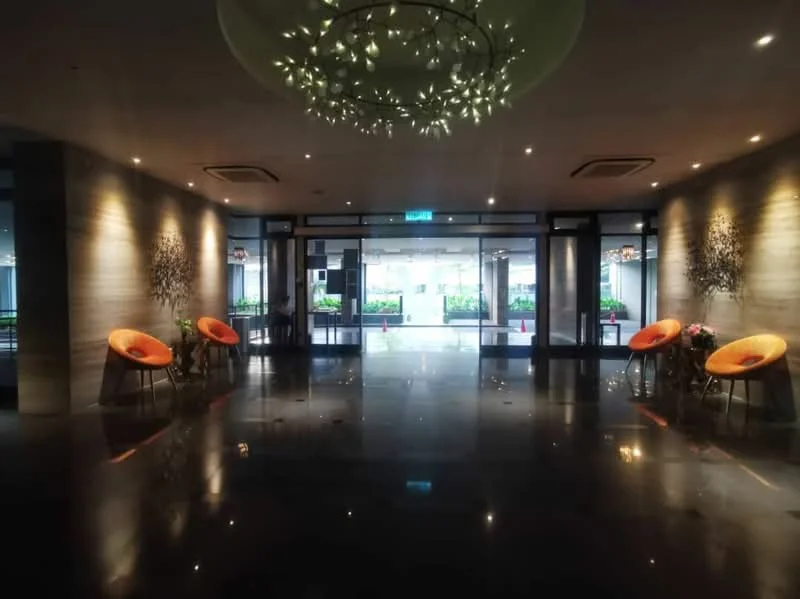 Room features: polished marble flooring, recessed downlights, chandelier with floral design, glass entrance doors, large windows allowing natural light, orange accent chairs, decorative wall art, indoor plants, modern reception area, high ceiling; style: modern; view: garden.
