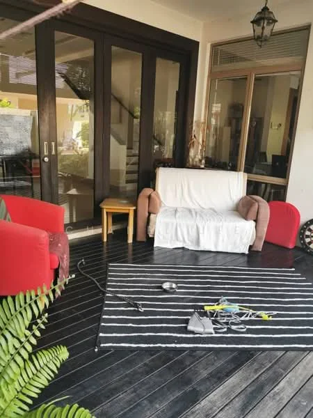 Room features: wooden flooring, red armchair, beige sofa with cover, striped area rug, wooden side table, indoor plants, large glass doors, natural light from windows, decorative lantern, various items on the floor; style: contemporary; view: garden.
