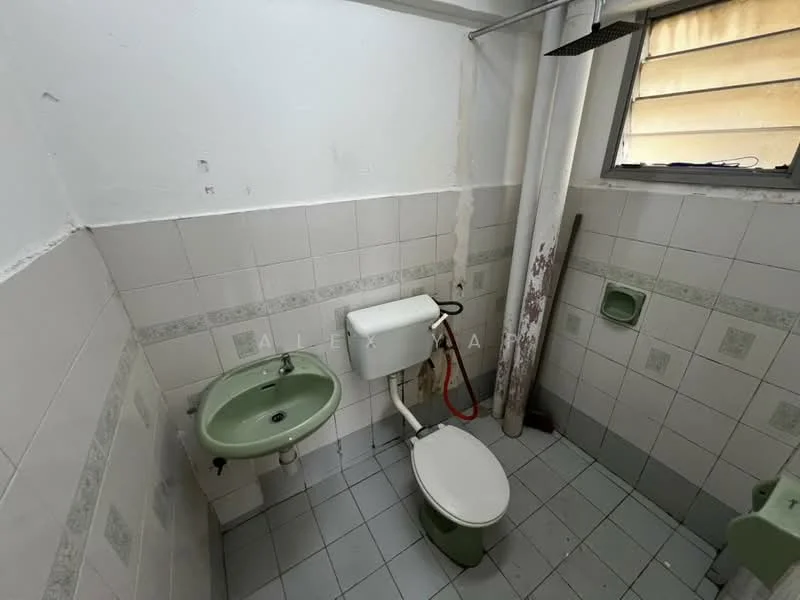 Bathroom features: white tiled walls, grey tiled flooring, green ceramic sink, white toilet, shower head, window with horizontal bars, wall-mounted faucet, toilet paper holder.