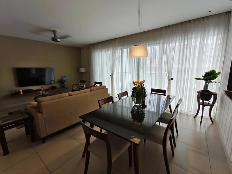 Dining features: glass dining table, 6 wooden dining chairs, pendant light fixture, floor-to-ceiling windows, sheer curtains, potted plant, neutral wall color, tile flooring; style: modern; view: garden. Living features: 3-seater fabric sofa in beige, wall-mounted TV, coffee table, side table, ceiling fan, decorative wall art; style: modern; view: garden.
