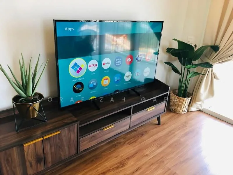 Living features: large flat-screen TV, wooden TV console with drawers, decorative potted plant, light-colored walls, wooden flooring, curtains, decorative basket, wall-mounted electrical outlet; style: modern.
