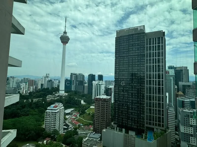 Exterior type: high-rise condominium; features: city skyline view, KL Tower visible, surrounded by urban landscape, glass facade, green park area in foreground, multiple high-rise buildings, cloudy sky; style: modern.