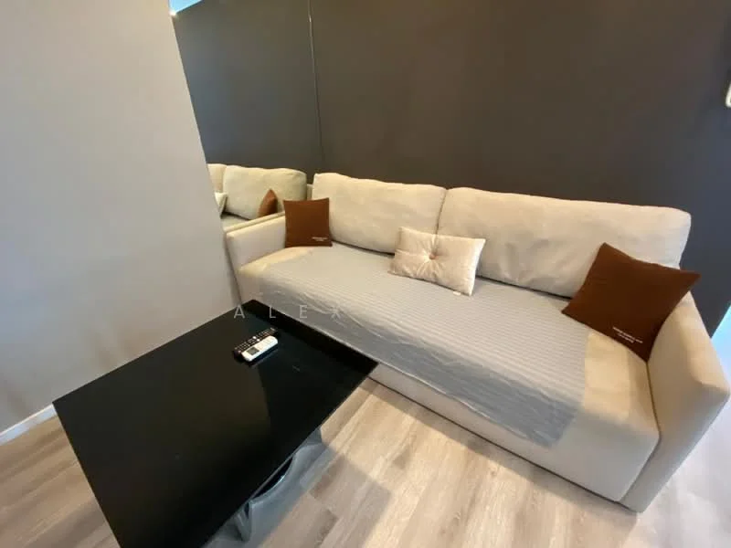 Living features: light grey fabric sofa, decorative cushions in brown, black coffee table, light wood flooring, dark accent wall, mirror on wall, neutral wall colour, minimalist decor; style: modern.