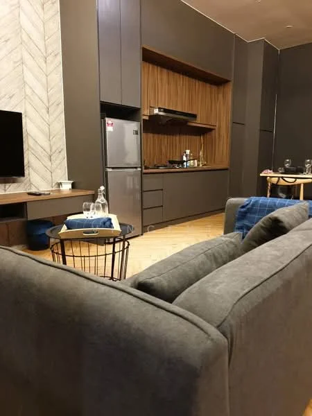 Living features: grey fabric sofa, wooden coffee table, flat-screen TV on wall-mounted console, stainless-steel fridge, wood cabinetry, open shelving, laminate flooring, decorative wall with herringbone pattern, recessed lighting, dining table with chairs, glassware on table; style: modern.