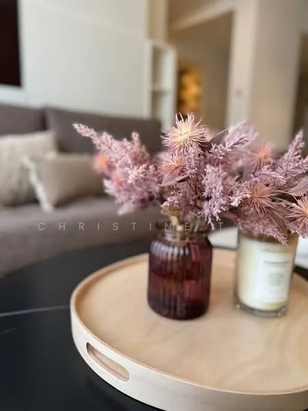 Room features: decorative vase with flowers, wooden serving tray, candle, soft furnishings in neutral tones, coffee table, textured fabric sofa, decorative pillows; style: modern.